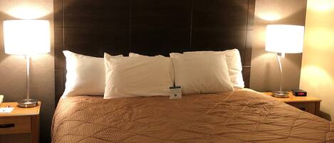 A hotel room with a large bed, two bedside lamps, a nightstand with a lamp, and a digital clock displaying 11:07.