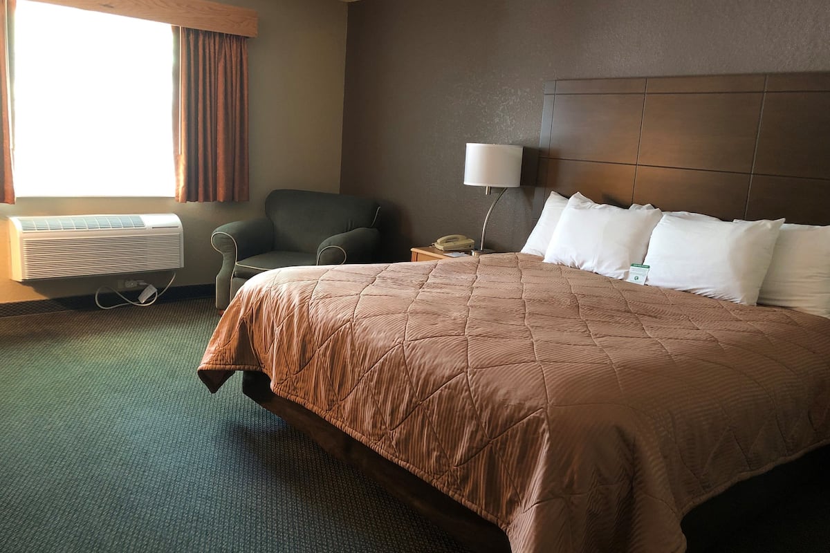 A hotel room with a large bed, a chair, a desk with a lamp, and a window with curtains.