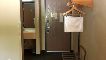 Ein Hotelzimmer mit Holztür, Spiegel, Waschbecken, Kleiderständer und einem Stuhl.