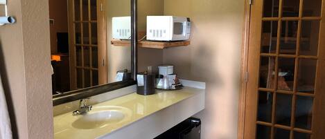 A bathroom with a sink, mirror, and a microwave on a shelf.
