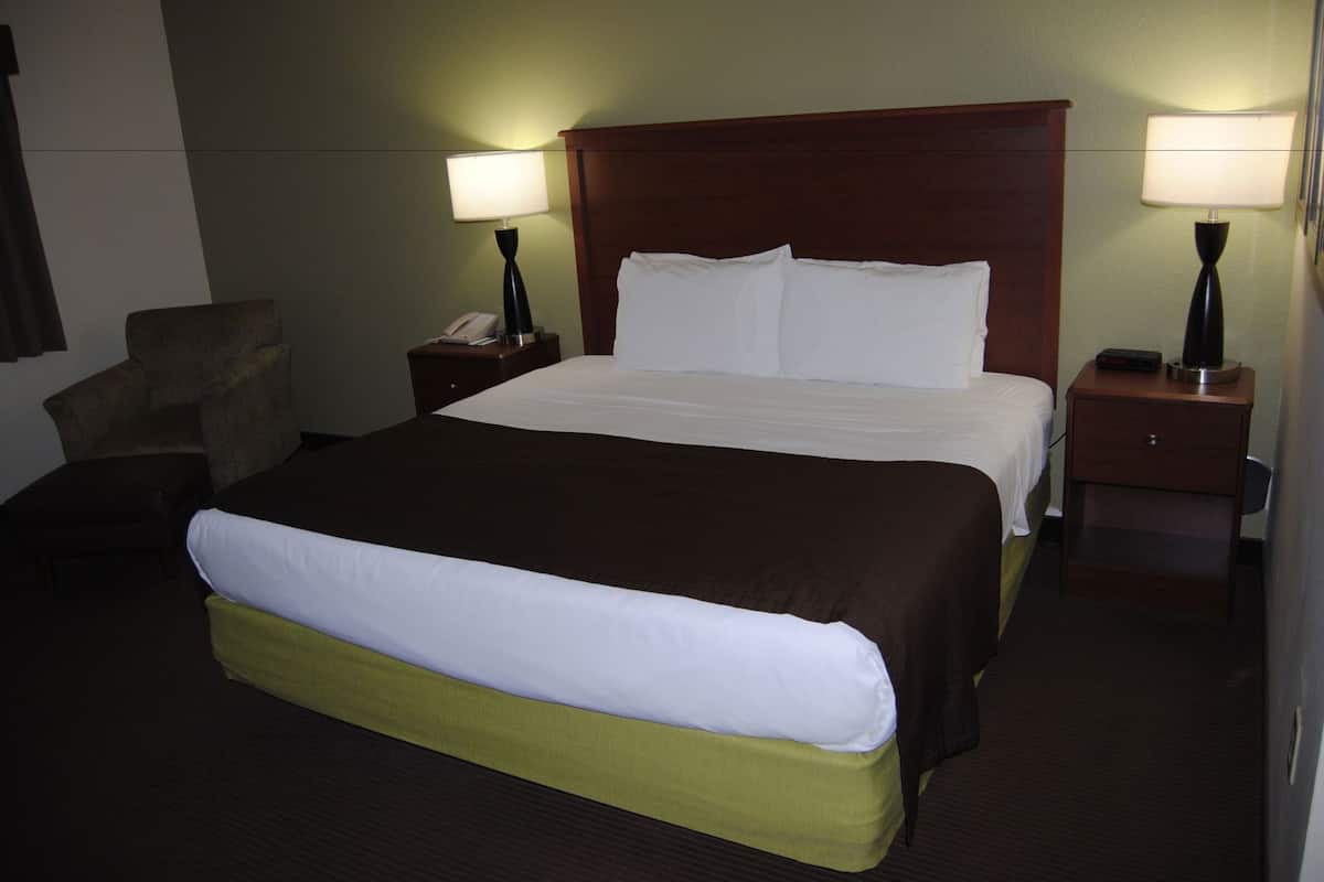 A hotel room with a large bed, two bedside tables with lamps, a chair, and a nightstand with a phone.