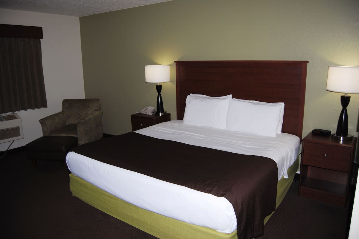 A hotel room with a large bed, two bedside tables with lamps, a chair, and a desk with a telephone.