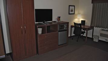 A hotel room with a wooden wardrobe, a desk with a computer, a microwave, a small refrigerator, and a chair.