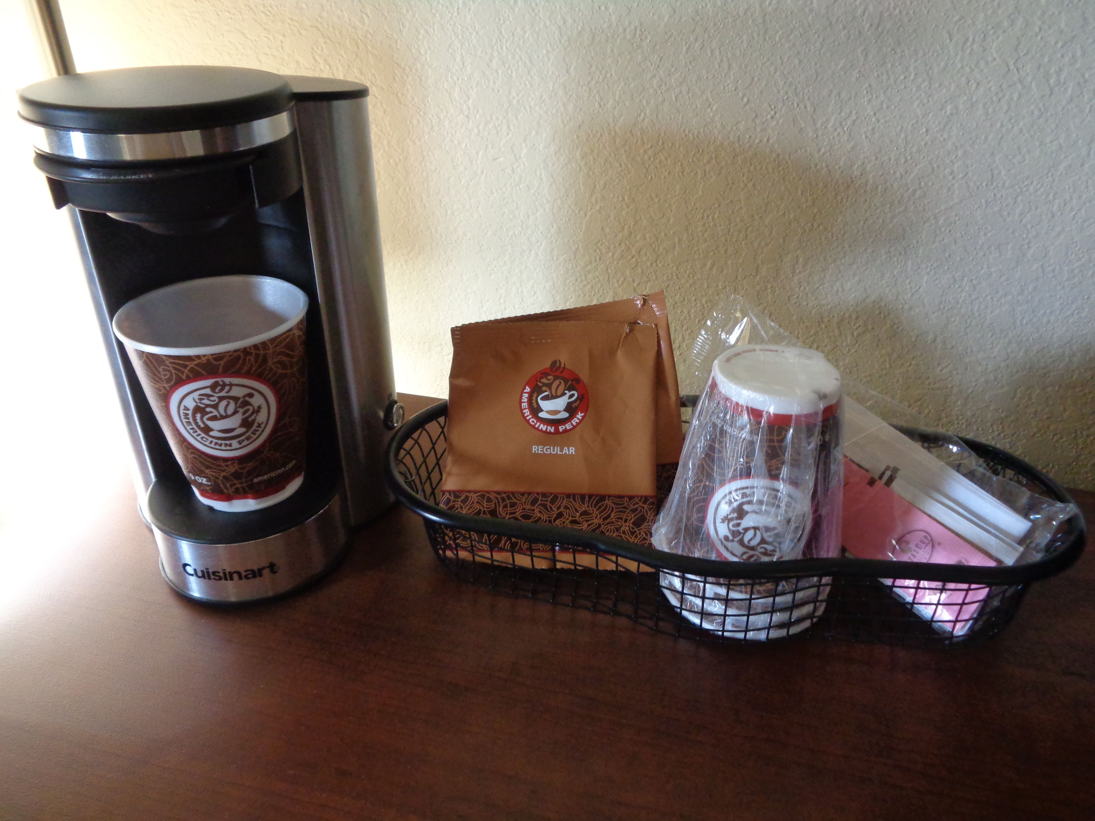 A coffee maker, a paper cup, a reusable coffee cup, a reusable mug, and a reusable water bottle on a table.