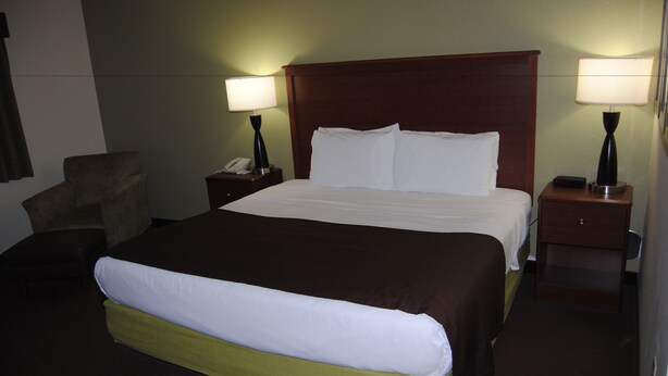Habitación de hotel con una cama grande, dos mesitas de noche con lámparas, una silla y una mesita con teléfono.