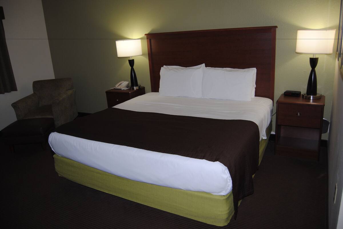 A hotel room with a large bed, two bedside tables with lamps, a chair, and a nightstand with a phone.