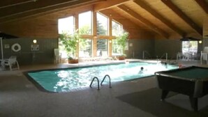 Una piscina interior con mesa de billar y sillones de descanso.