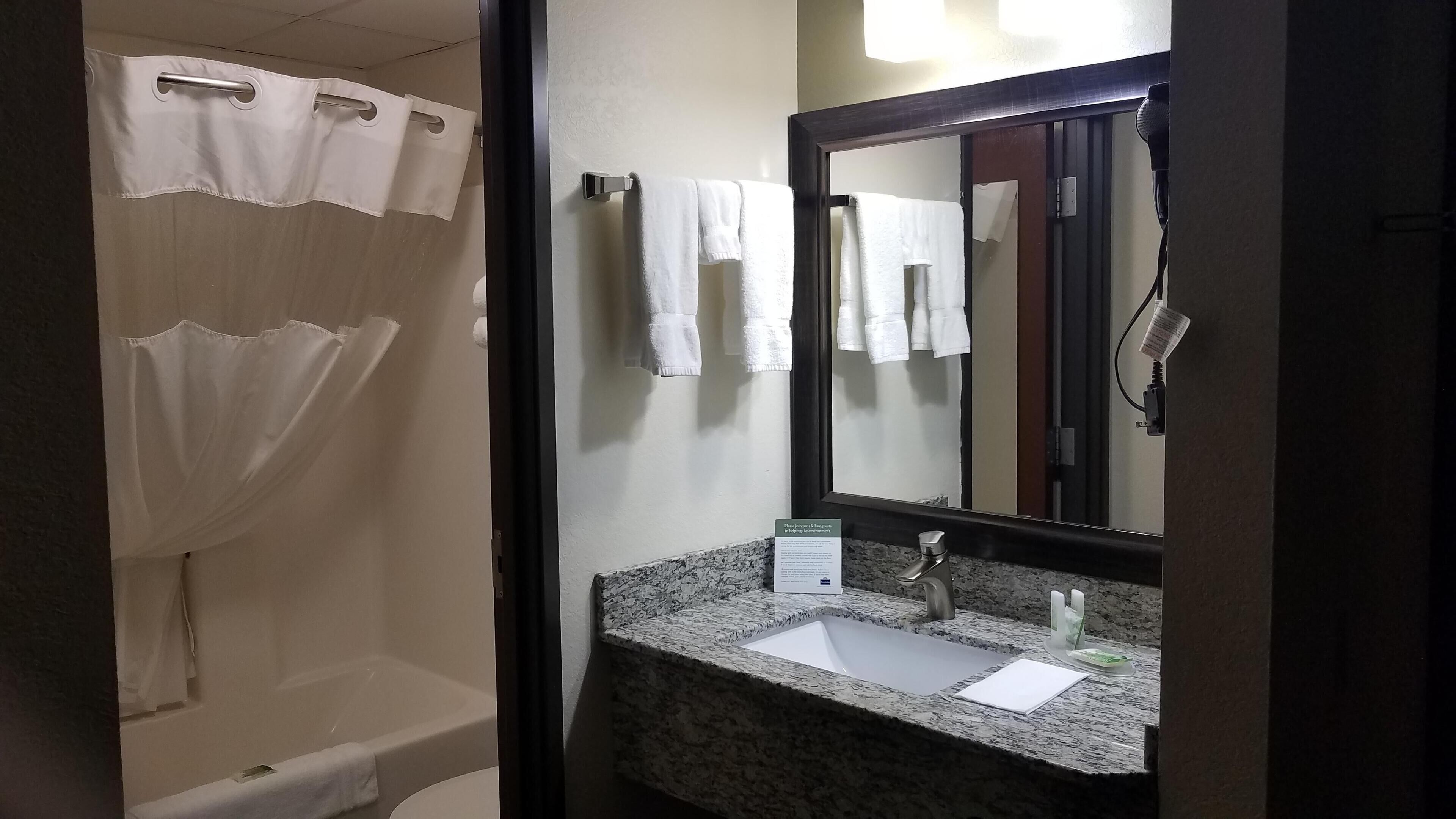 Un baño con cortina de ducha, un lavabo con espejo y un cartel en la encimera.