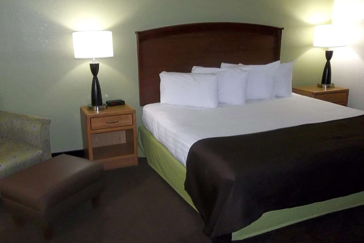 A hotel room with a bed, two bedside tables with lamps, a chair, and a small table.