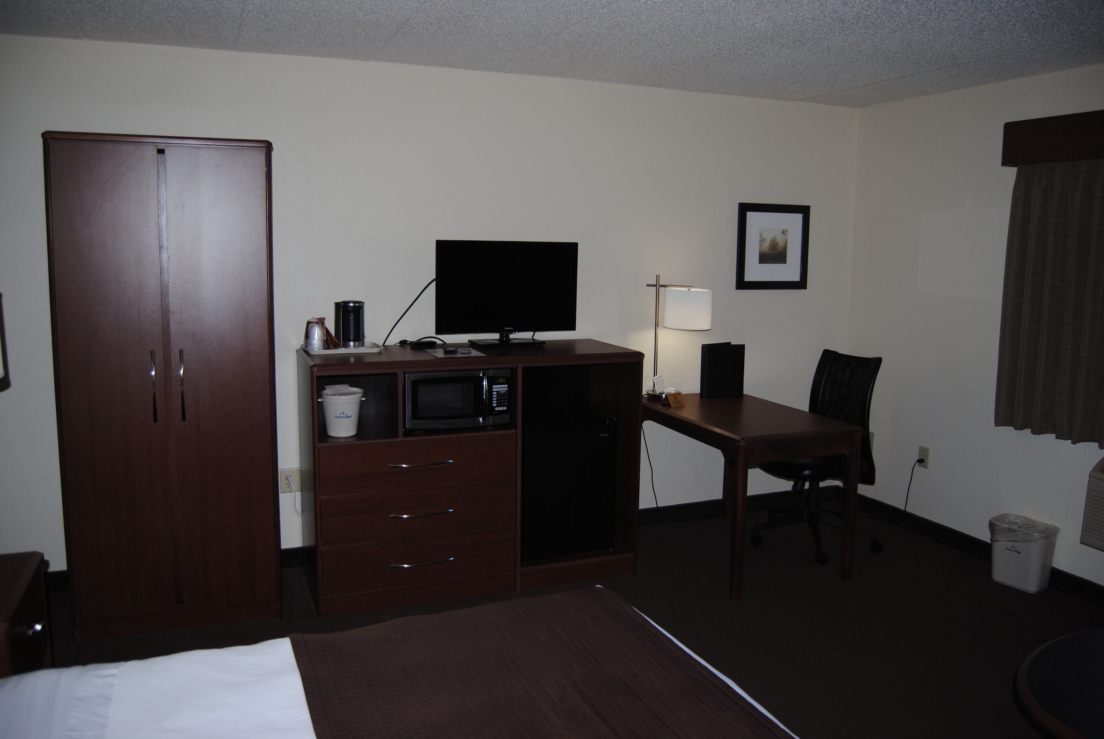 Una habitación de hotel con cama, escritorio, televisor, microondas, lámpara y armario.