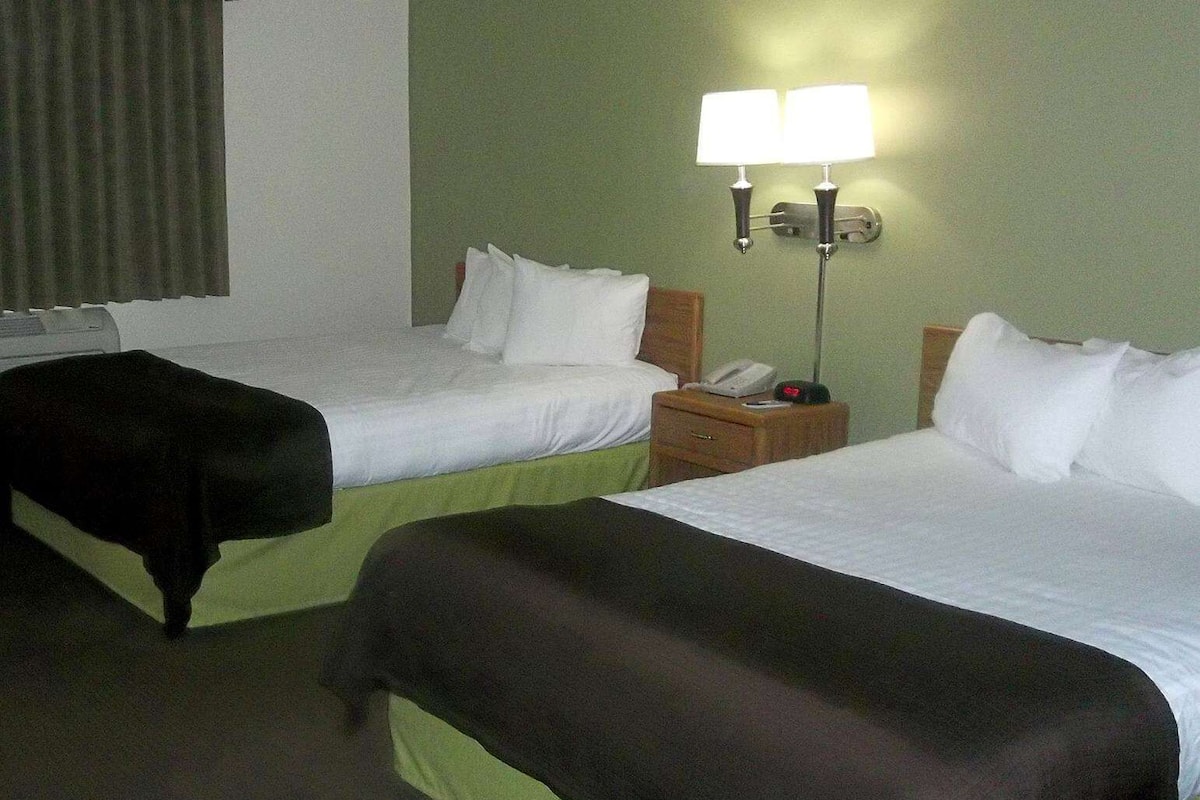A hotel room with two beds, a nightstand with a phone, and a wall-mounted lamp.