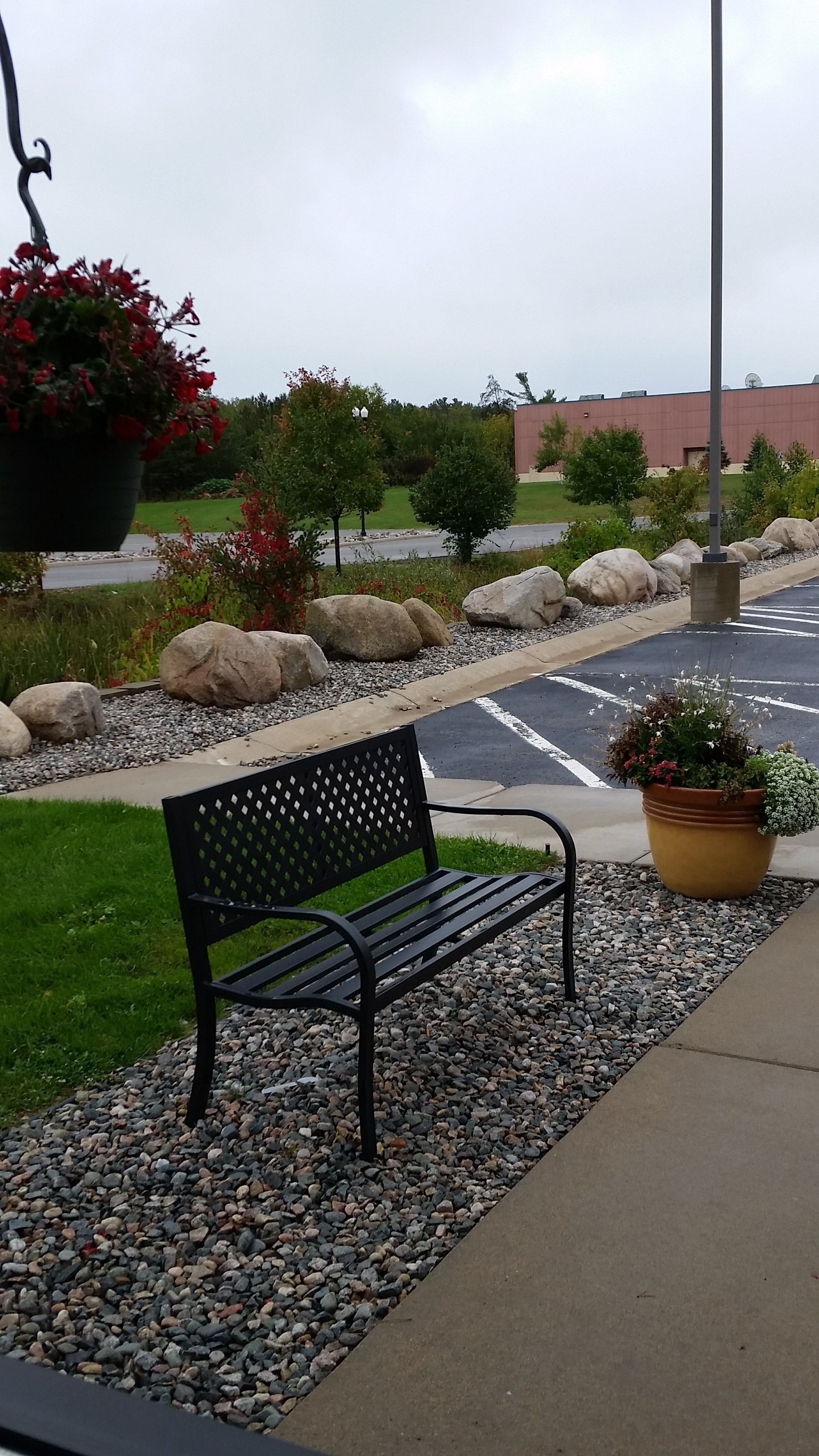 A bench with a metal frame and backrest, positioned on a gravel path with a potted plant nearby.