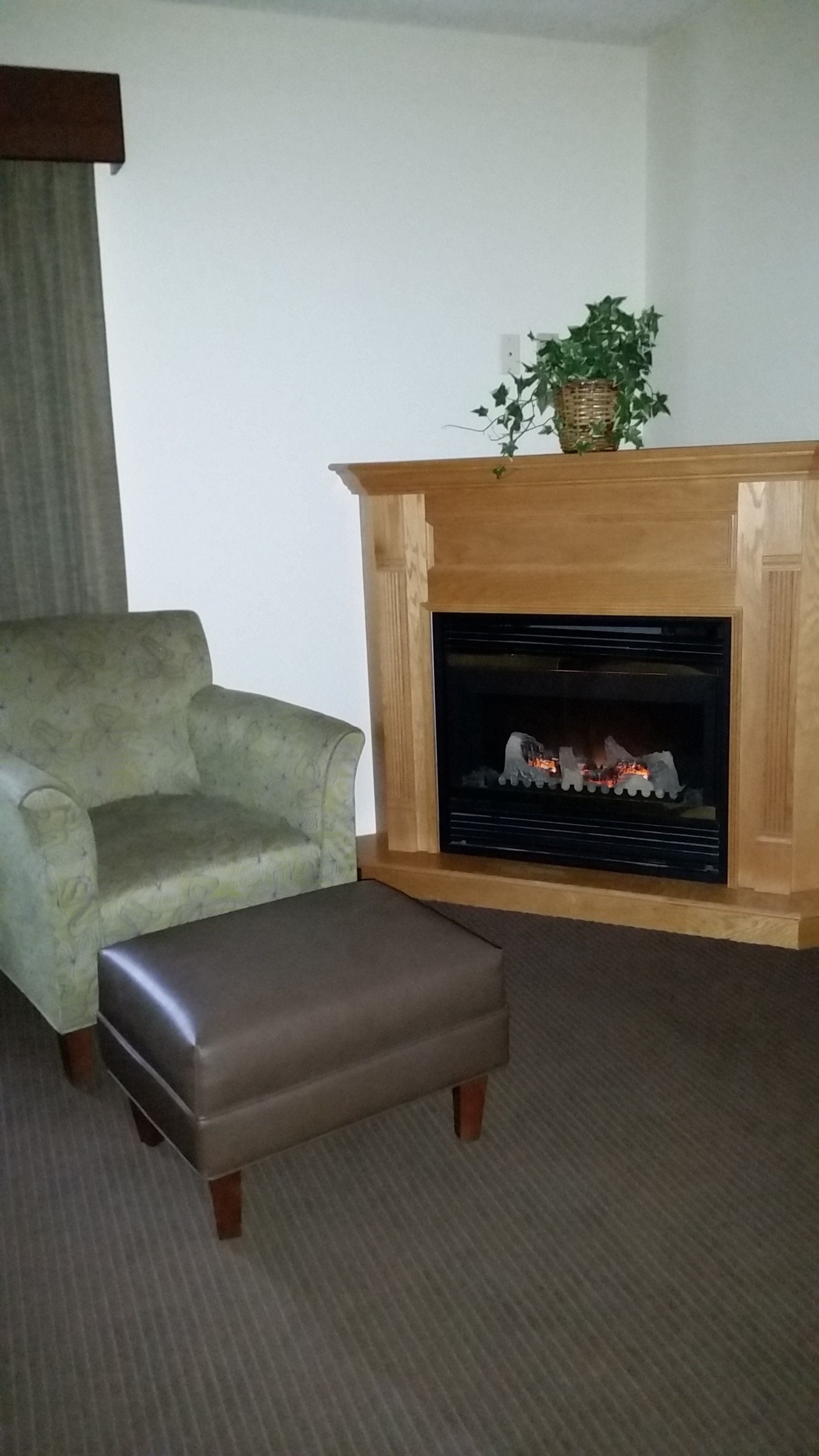 A living room with a fireplace, a green armchair, and a brown ottoman.