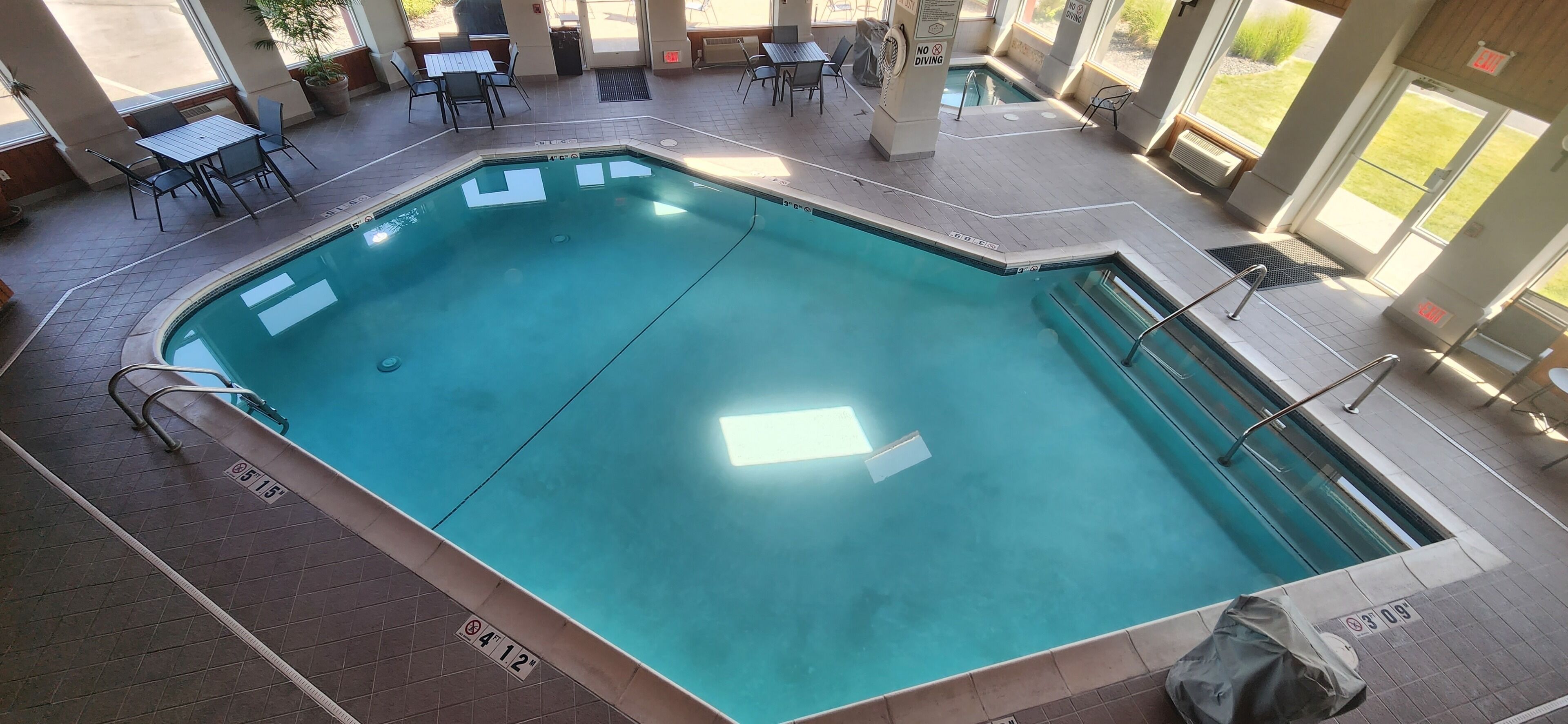 Piscina interior rectangular con agua cristalina, rodeada por una solana con baldosas y mobiliario de exterior.