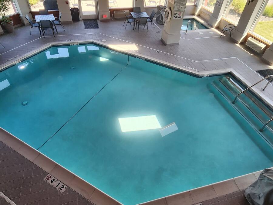 A rectangular indoor pool with clear water, surrounded by a tiled deck and outdoor seating.