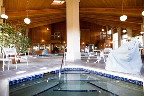 An indoor swimming pool with tiled walls and a wooden ceiling, surrounded by lounge chairs and tables.