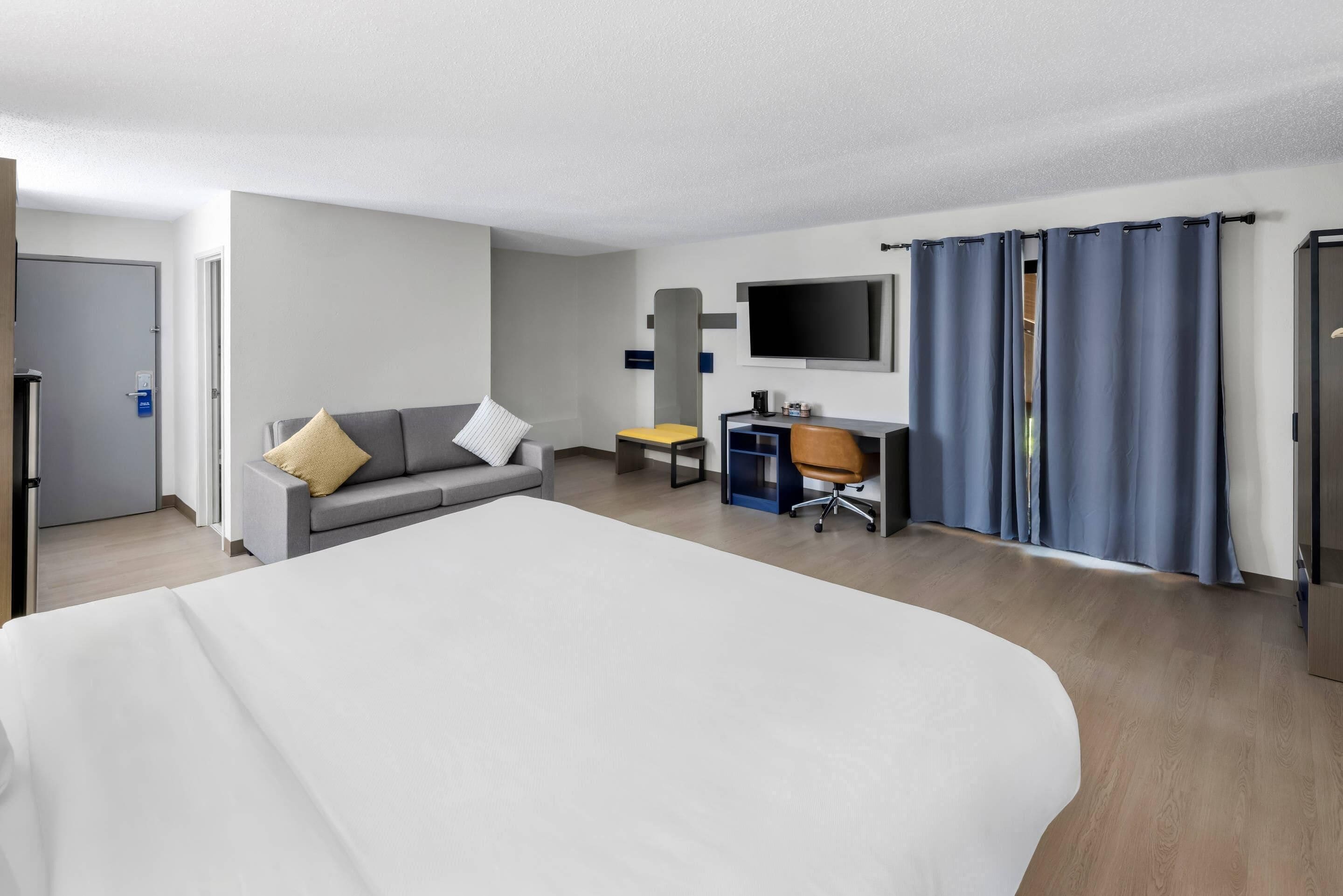 A hotel room with a large bed, a sofa, a desk, a television, and a wardrobe.