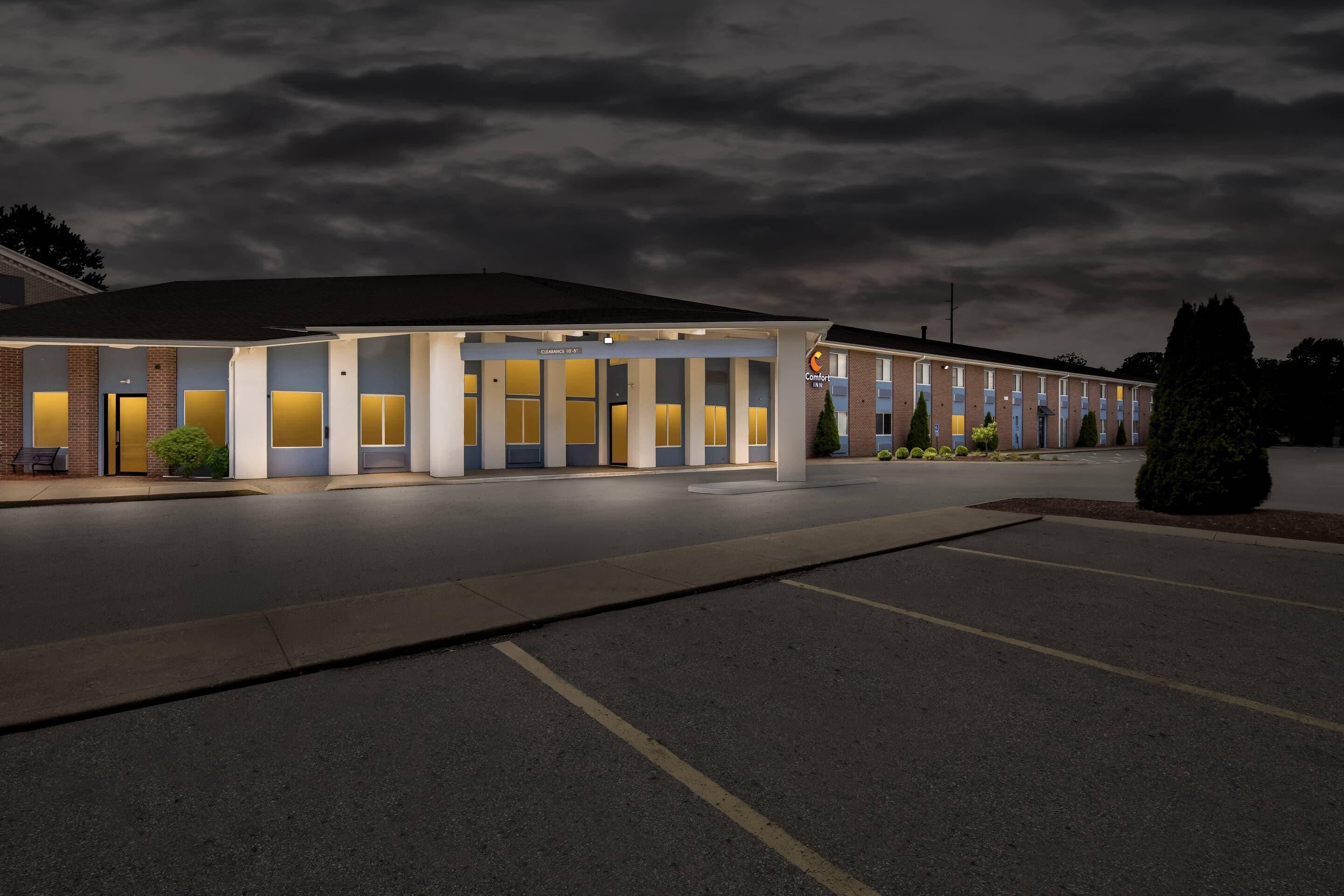 A motel with a row of rooms, a covered parking area, and a well-lit facade.