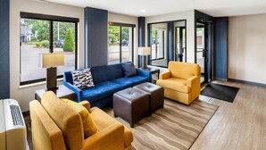 A hotel lobby with a blue sofa, a yellow armchair, and a brown ottoman. There are large windows with a view of the street. - Comfort Inn Mount Vernon Downtown (Mount Vernon)