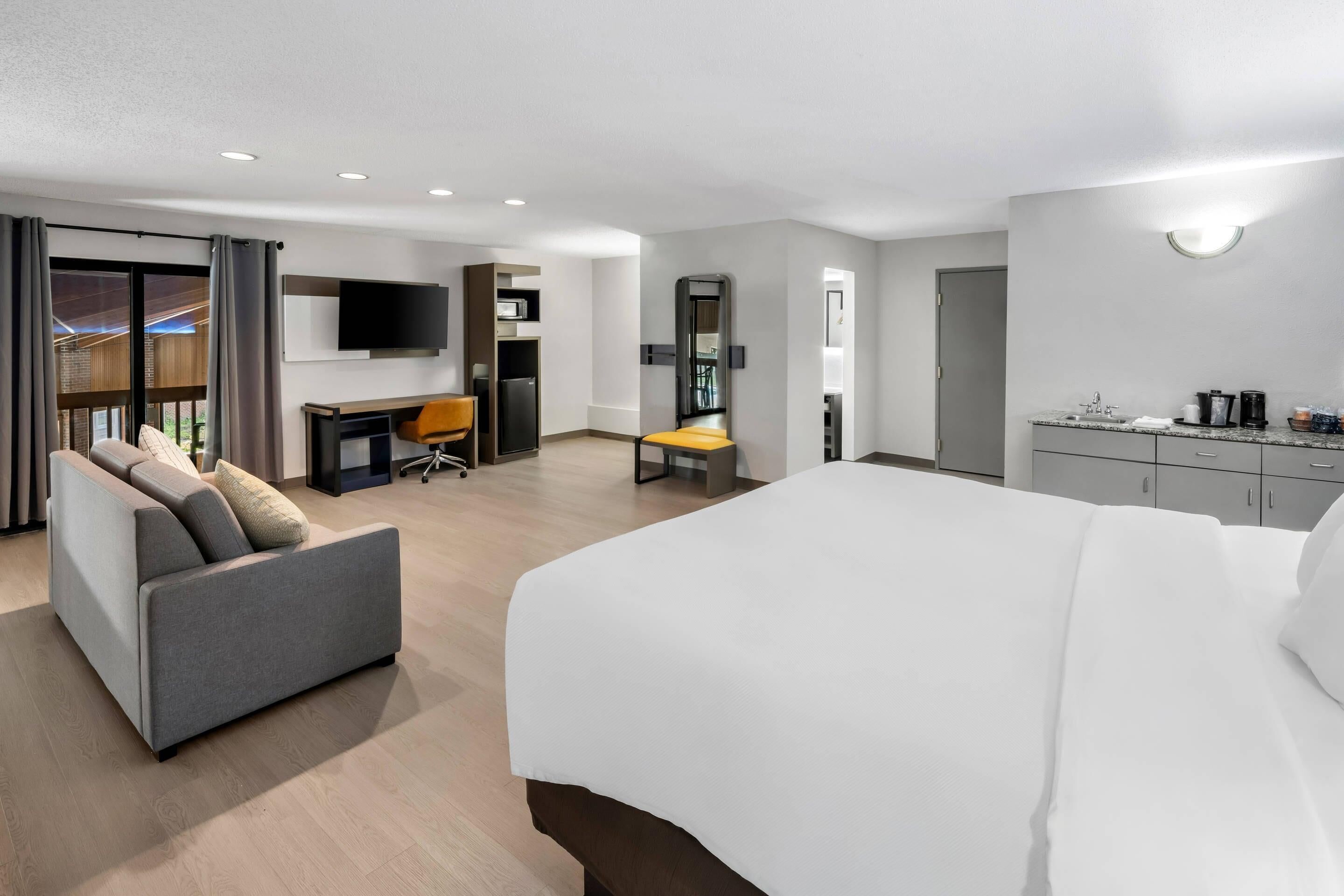 Habitació d'hotel moderna amb un llit gran, un sofà, un escriptori i una televisió.