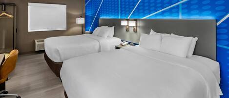 A hotel room with two beds, a desk, a chair, a window, and a wall with a geometric pattern.