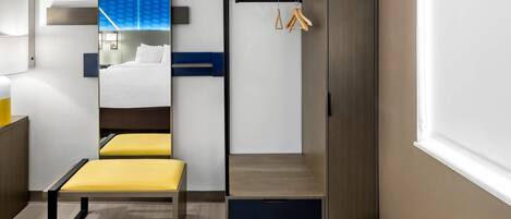 Habitación de hotel con cama, un banco, armario, espejo y perchero.