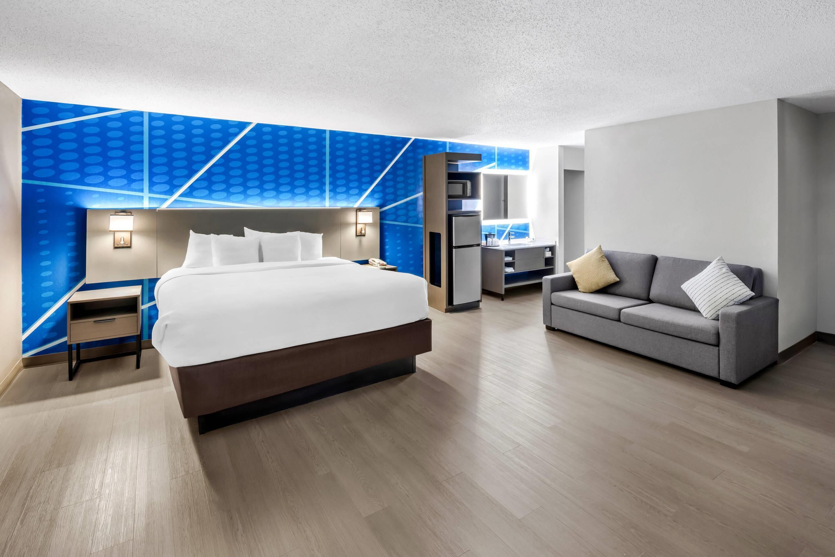 Habitación de hotel moderna con una cama grande, un sofá, un escritorio y una pared de acento azul.