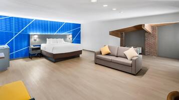 A modern hotel room with a bed, a sofa, a desk, and a blue accent wall.