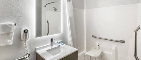 A modern bathroom with a white sink, a mirror, a handheld showerhead, and a grab bar.