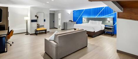 Una habitación de hotel moderna con sofá, cama, escritorio y espejo.