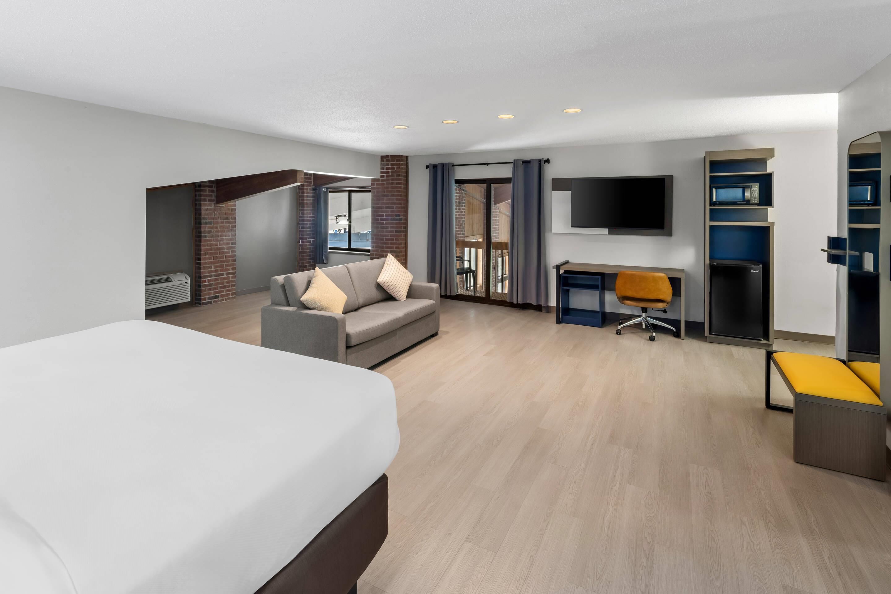 A modern hotel room with a large bed, a sofa, a desk, and a TV.