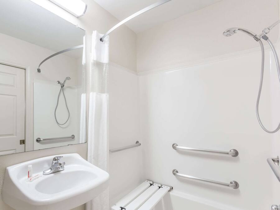 Un bagno moderno con un lavandino bianco, un soffione a mano e maniglie di sostegno.
