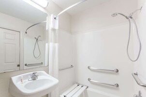 Un baño moderno con lavamanos blanco, ducha de mano y barras de apoyo.