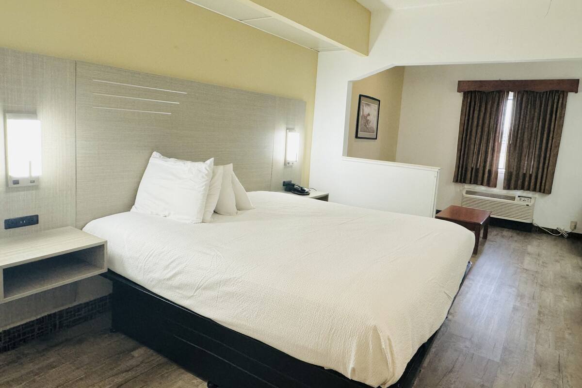 A hotel room with a large bed, bedside tables, a desk, and a window with curtains.
