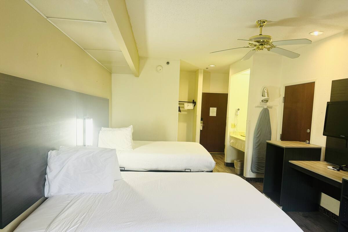 A hotel room with two beds, a ceiling fan, a TV, and a bathroom visible through an open door.