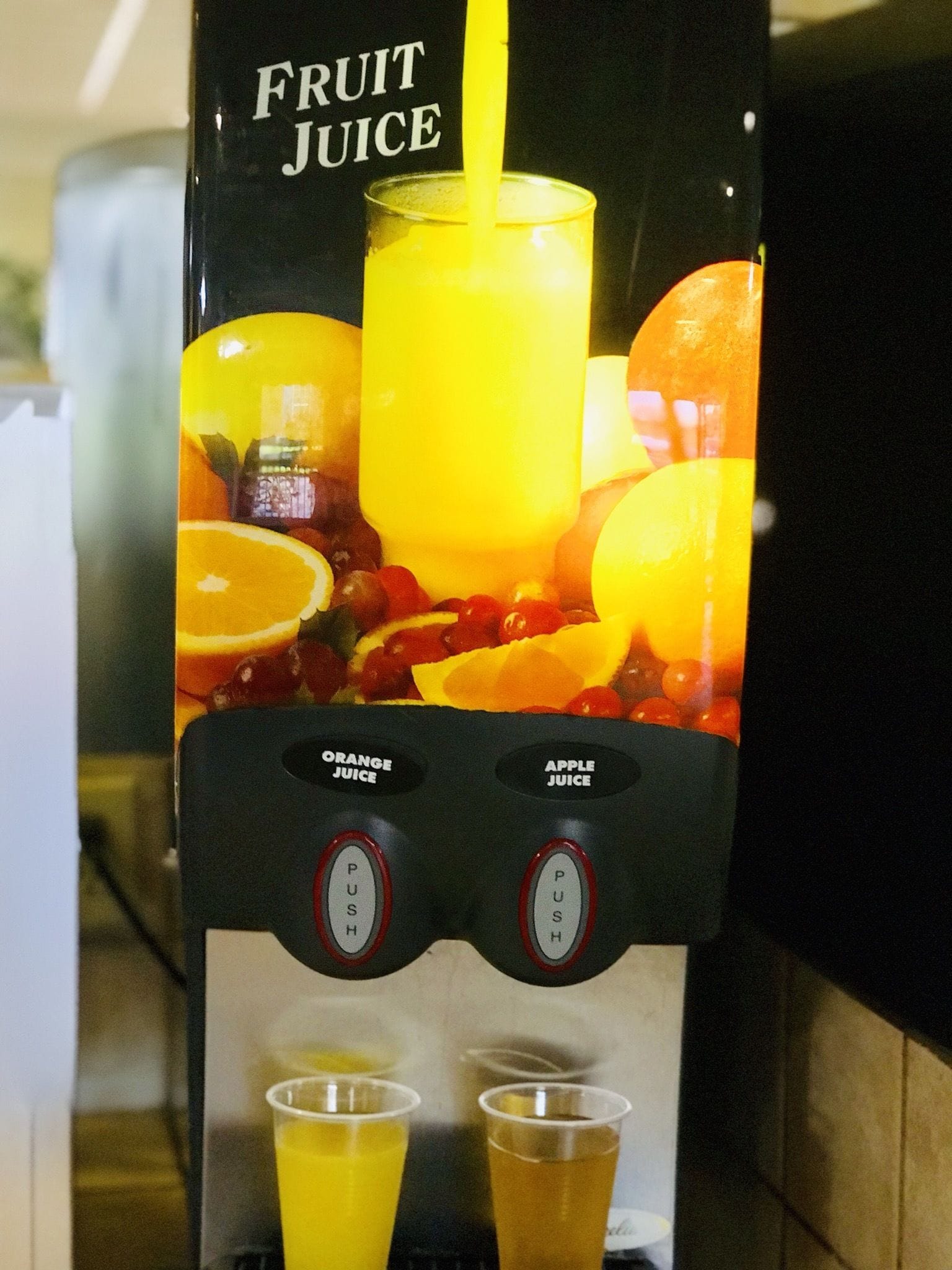 Un distributore di succo di frutta con due pulsanti etichettati 'Orange Juice' e 'Apple Juice' e due bicchieri pieni di succo.
