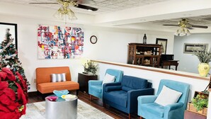 A living room with a Christmas tree, blue armchairs, an orange sofa, a coffee table, and a large abstract painting. - America's Best Inn and Suites Flowood (Flowood)