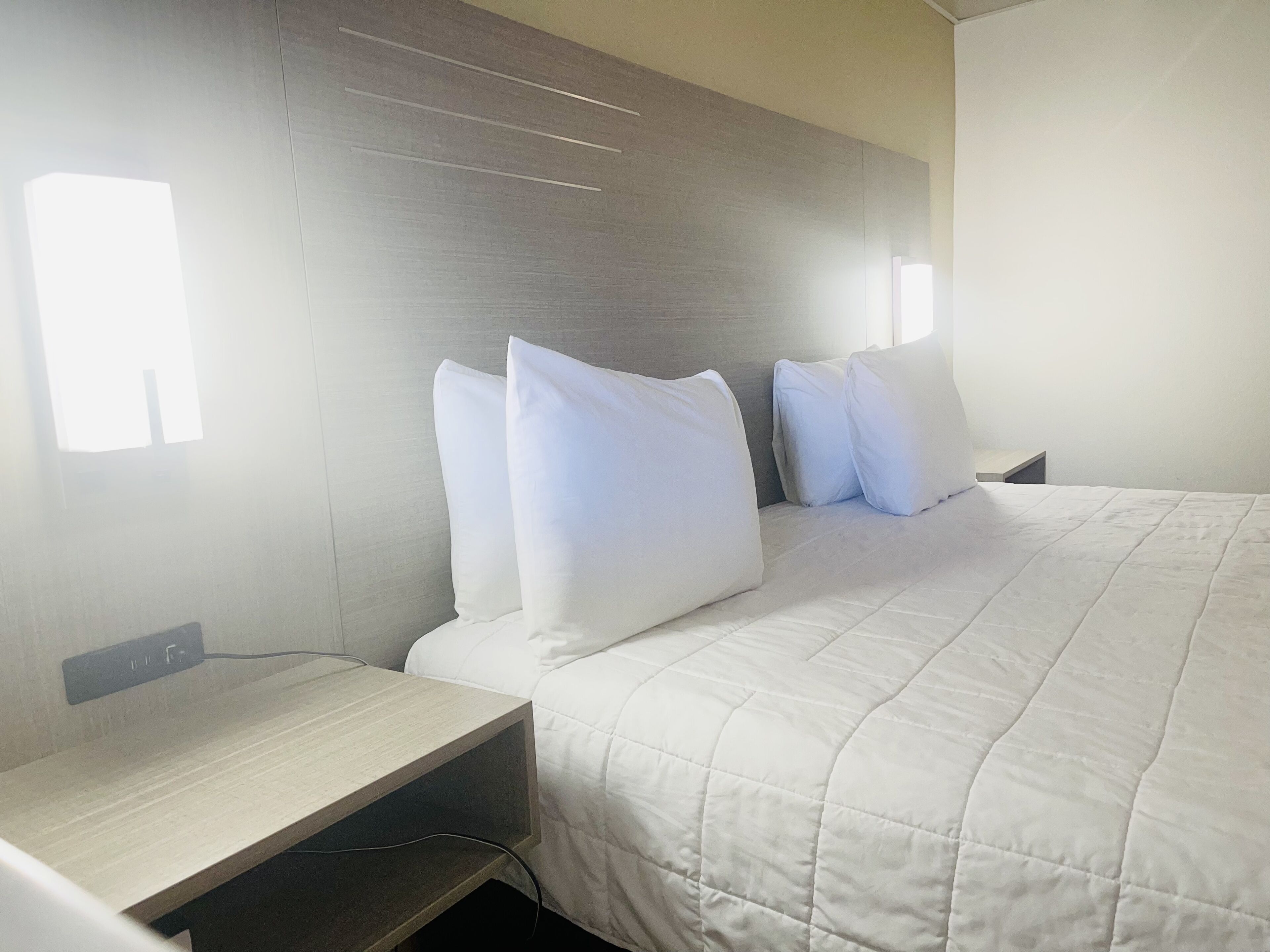 A hotel room with a bed, a bedside table, and a wall-mounted light fixture.