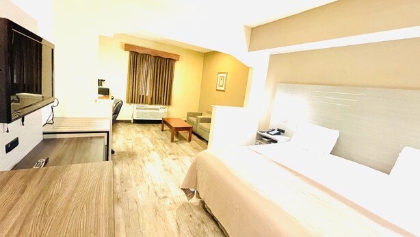 A hotel room with a bed, a desk, a chair, a sofa, and a television. - America's Best Inn and Suites Flowood (Flowood)