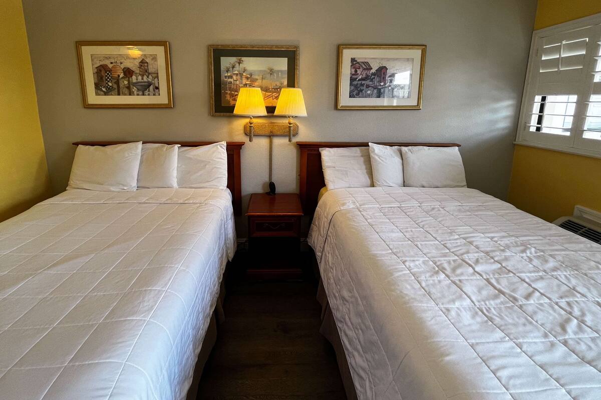 A hotel room with two beds, a nightstand with a lamp, and three framed pictures on the wall.