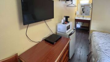 A compact hotel room with a flat-screen TV mounted on the wall, a small kitchenette with a microwave, and a bed with a patterned bedspread.