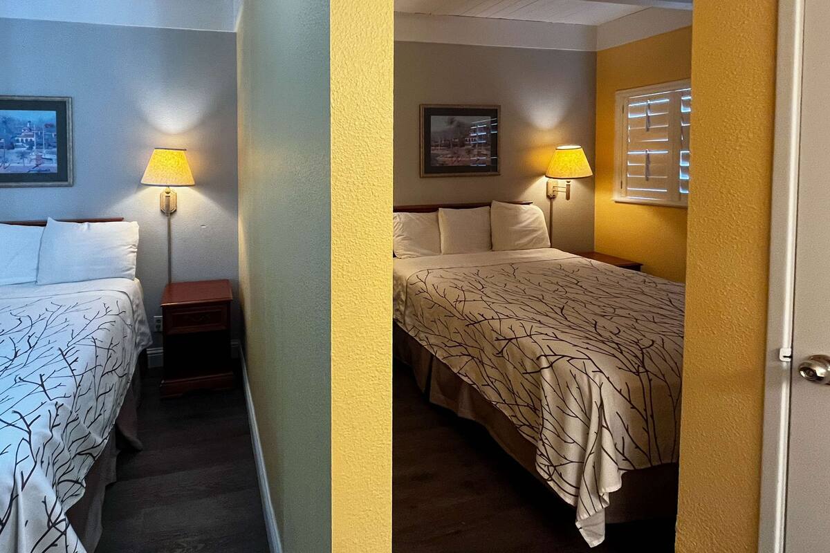 A hotel room with two beds, each with a lamp, a small table, and a framed picture on the wall.