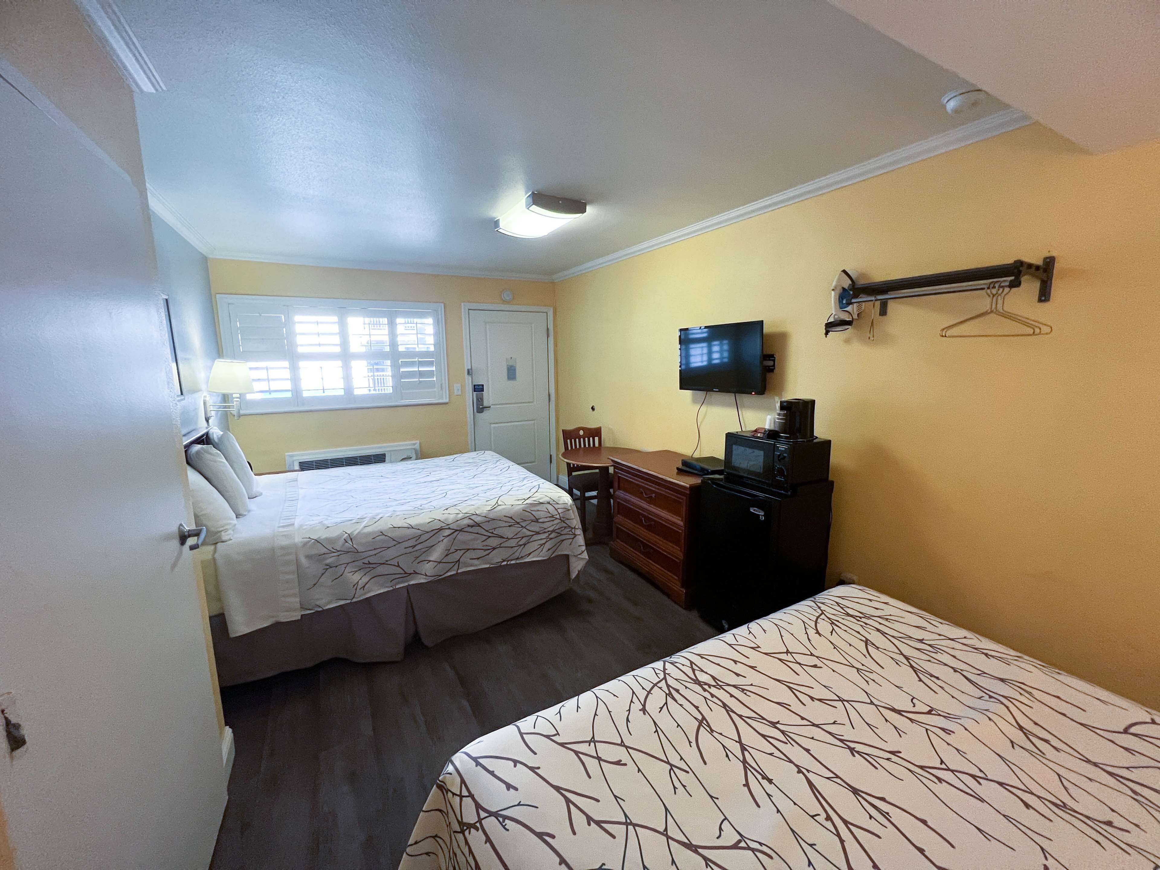Quarto de hotel com cama, escrivaninha com computador, televisão e micro-ondas.