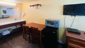 A compact hotel room with a kitchenette, a dining table with two chairs, a microwave, a TV mounted on the wall, and a small cabinet. - Motel 6 San Francisco, CA - Fisherman's Wharf (San Francisco)