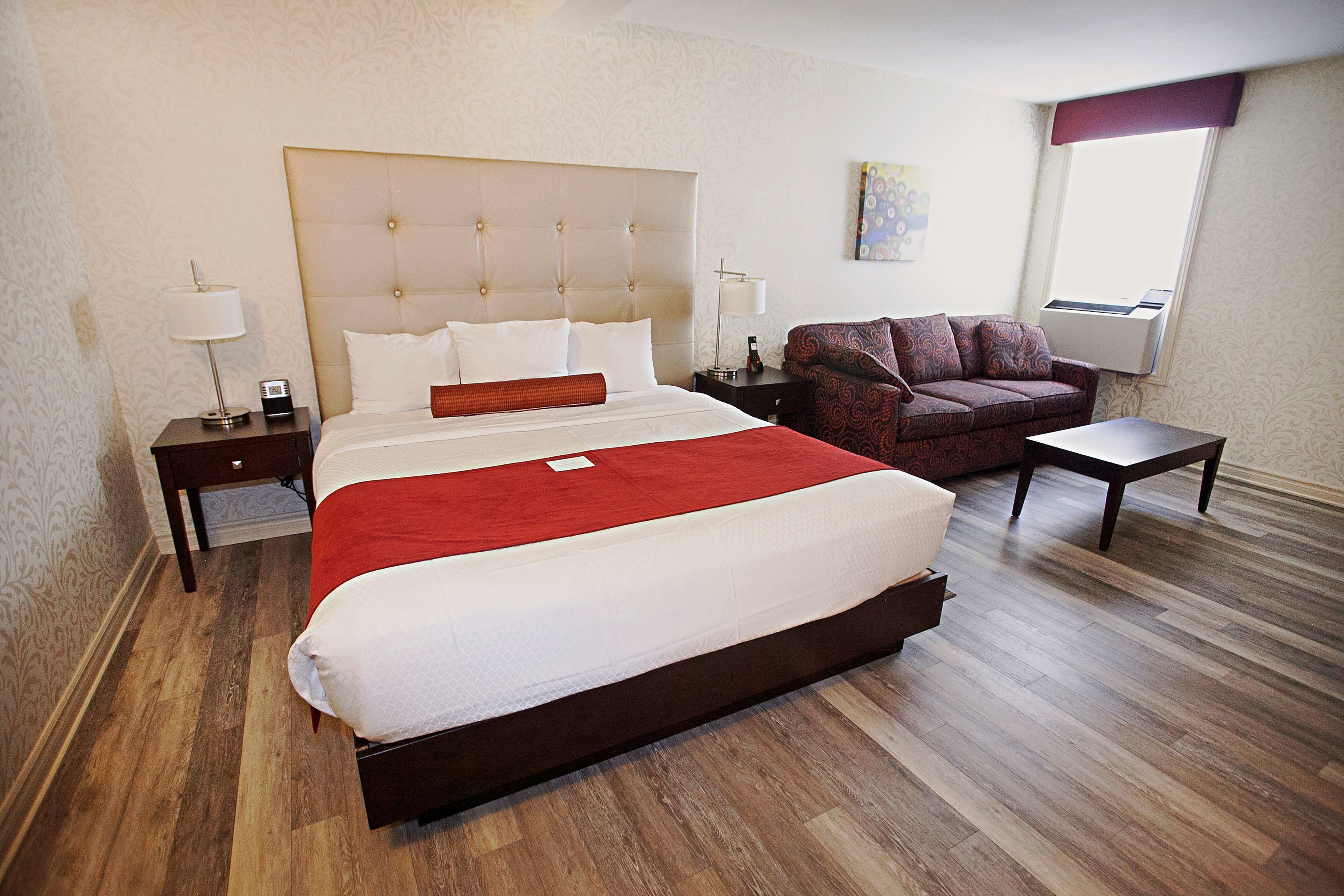 A hotel room with a large bed, a sofa, a small table, and a nightstand.