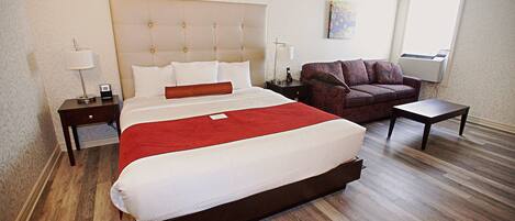 A hotel room with a large bed, a sofa, a small table, and a nightstand.