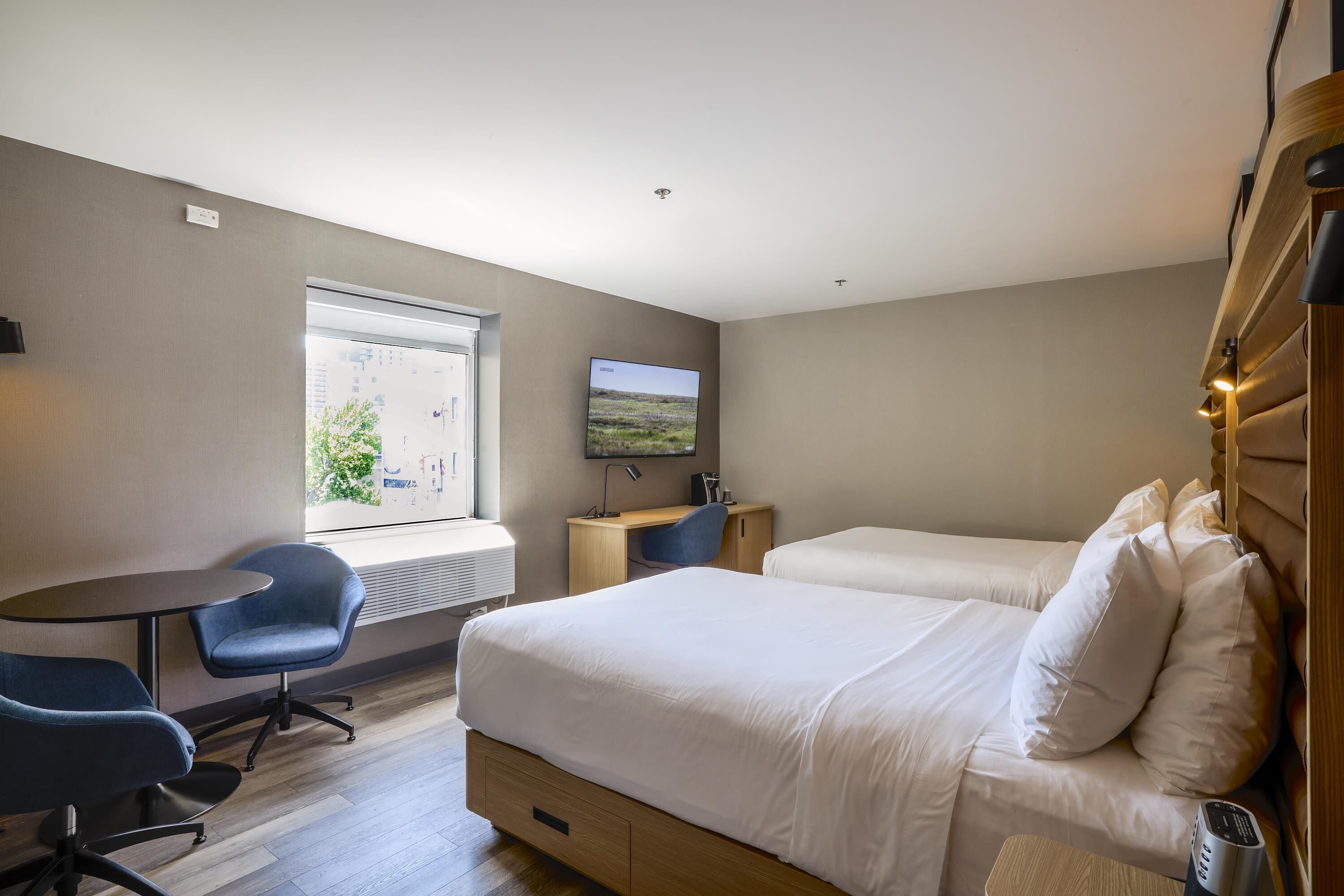 A hotel room with two beds, a desk, a chair, a TV, and a window with a view.