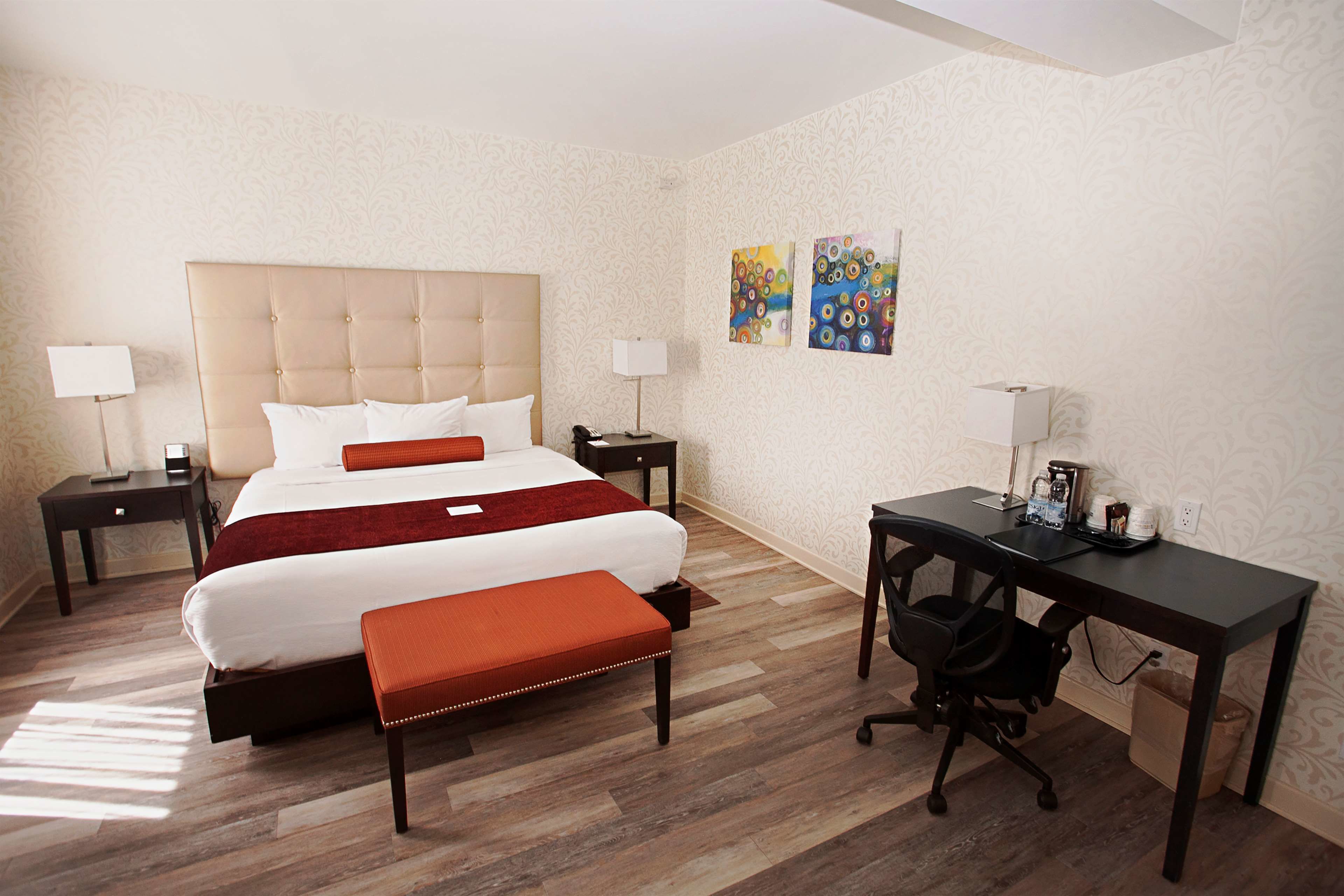 A hotel room with a large bed, a desk, and a chair. There are two nightstands with lamps and a trash can.