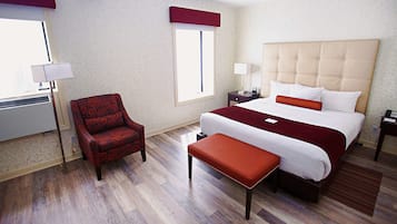 Ein Hotelzimmer mit einem großen Bett, einem roten Sessel, einer Bank und einem Fenster mit Blick.