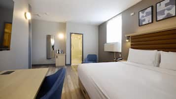 Une chambre d’hôtel comprenant un lit, un bureau, une chaise, un miroir, une porte donnant accès à une salle de bain et une lampe fixée au mur.